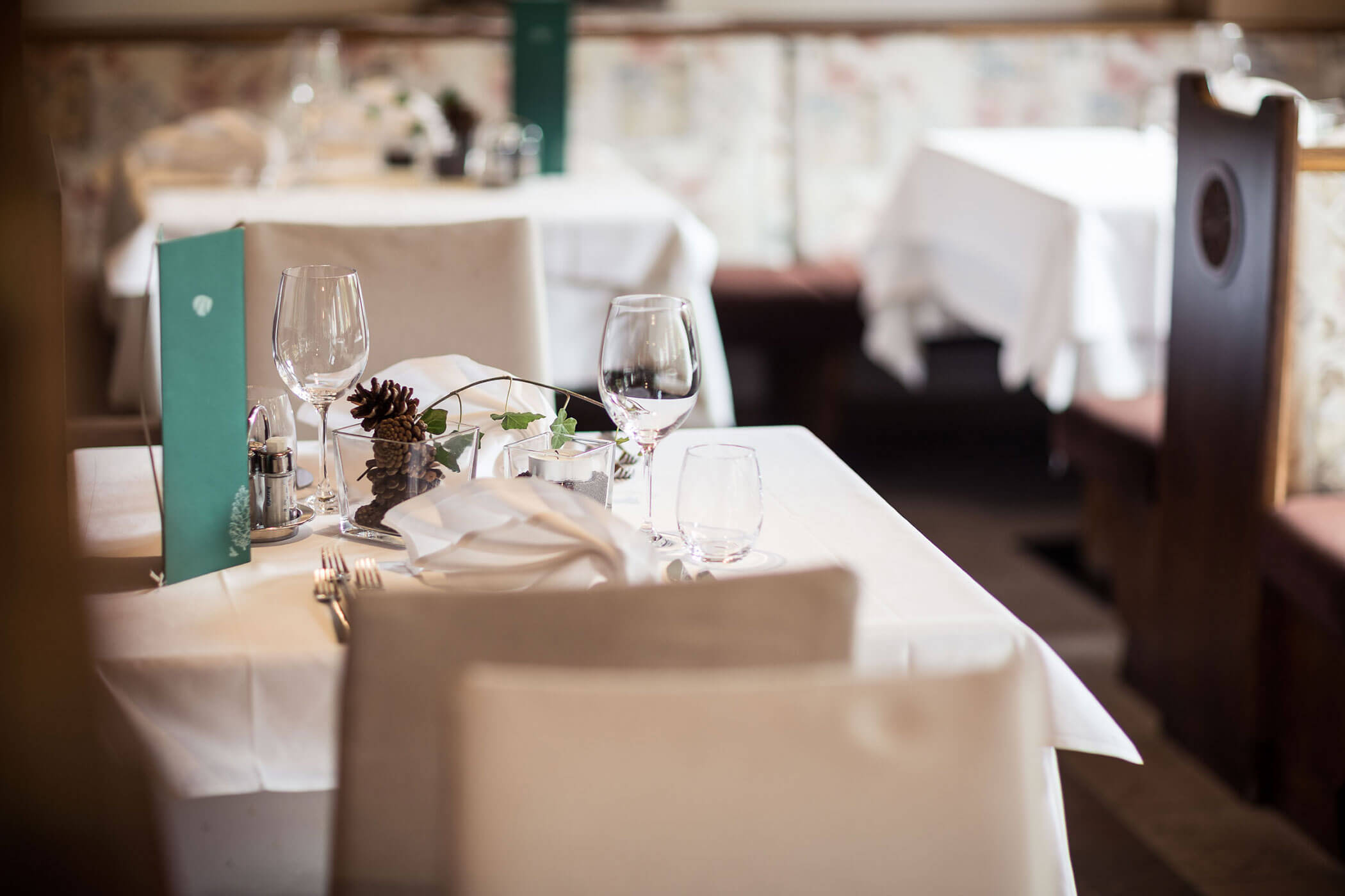 Weiß gedeckter Tisch mit Gläsern, Besteck, Servietten und Menü - Hotel Alpenhof