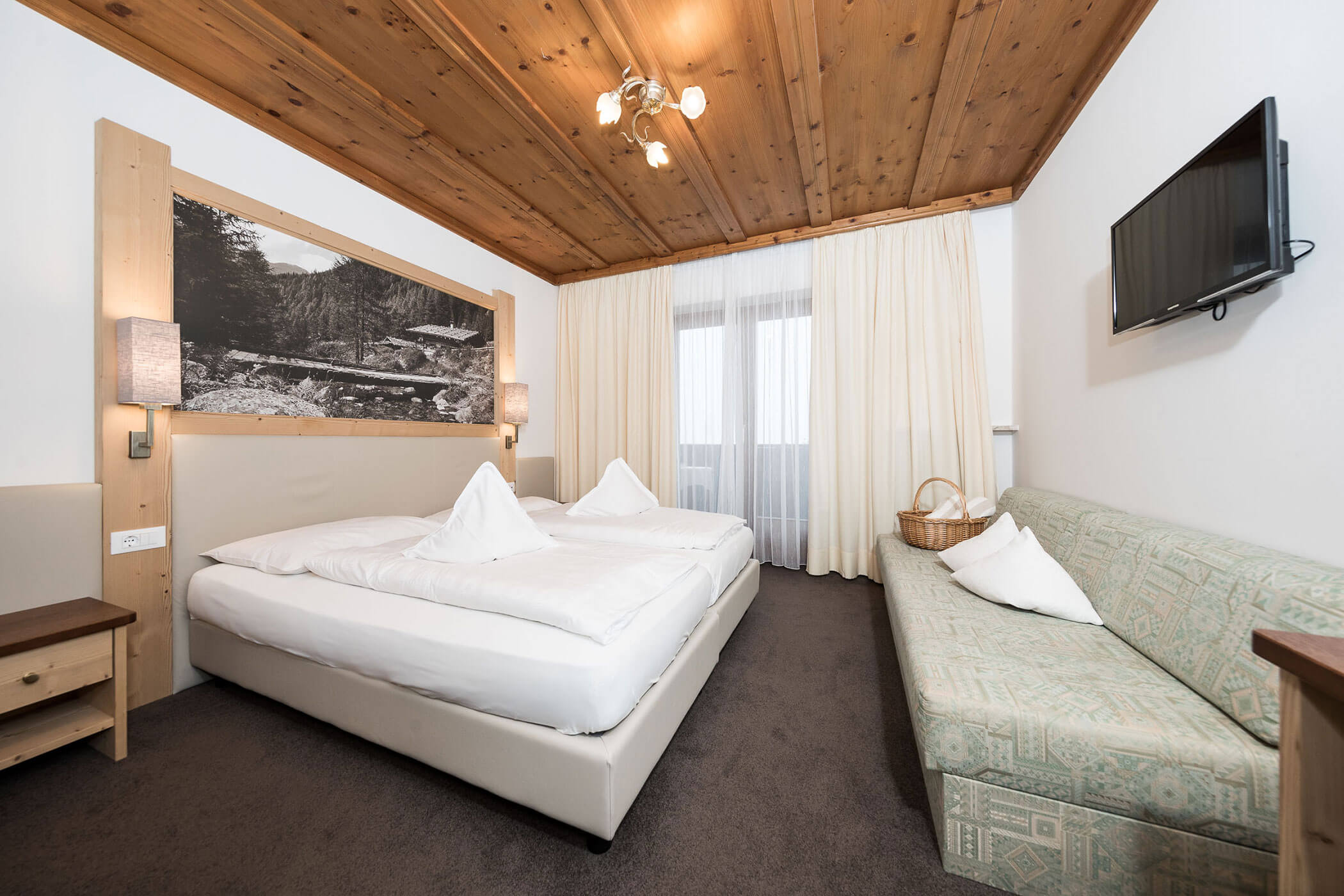 Hotelzimmer mit Doppelbett, Couch und TV darüber - Hotel Alpenhof