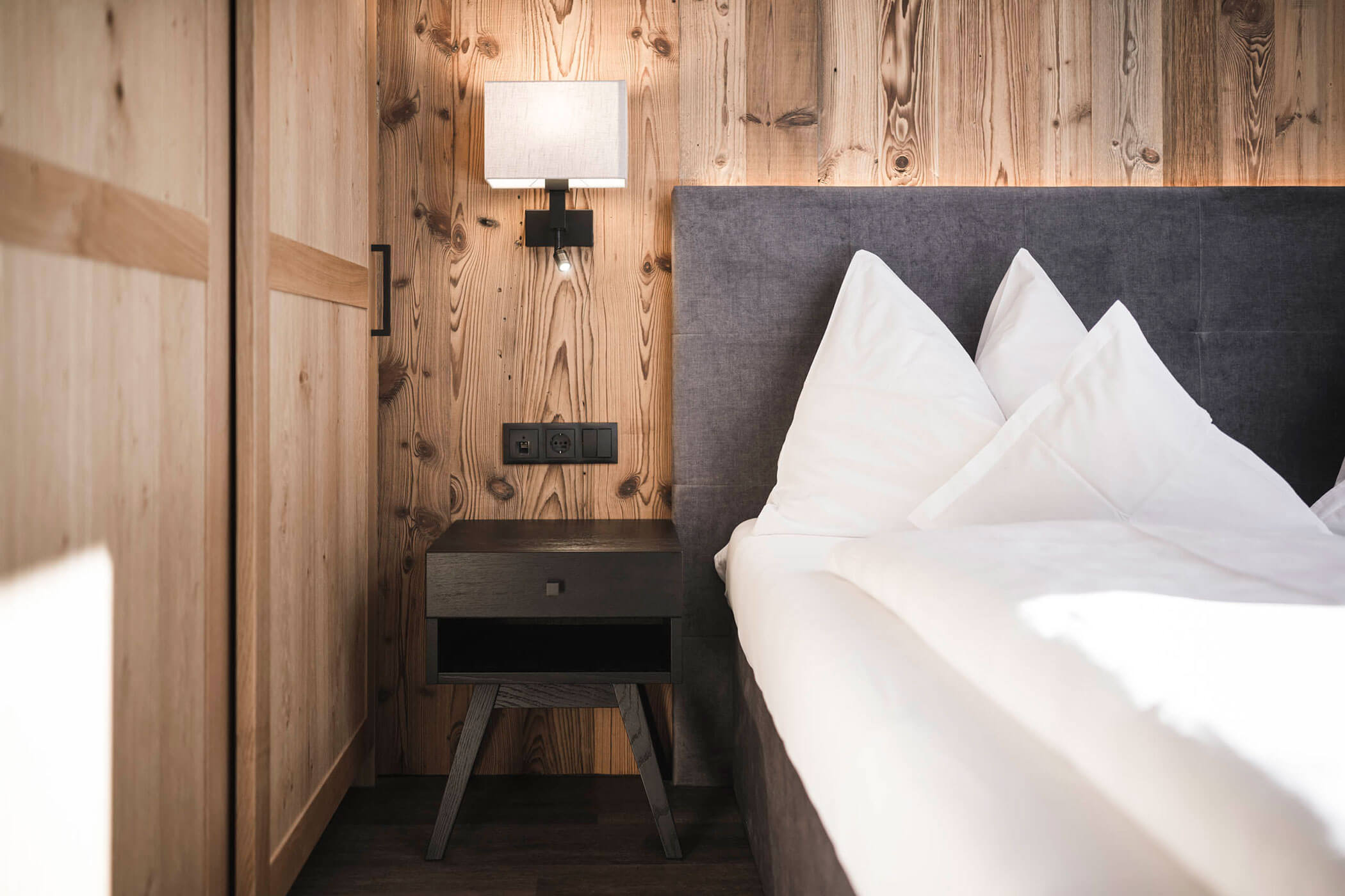 Doppelbett im Holzschlag Zimmer mit schwarzem Nachttisch und einem gemütlichem Nachtlicht - Hotel Alpenhof