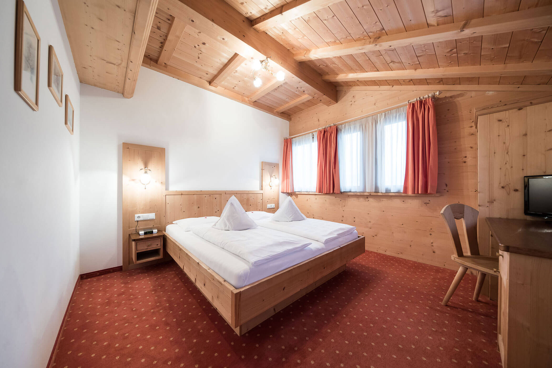 Die Spitzen Suite mit Doppelbett, rotem Teppichboden und Holzschreibtisch - Hotel Alpenhof