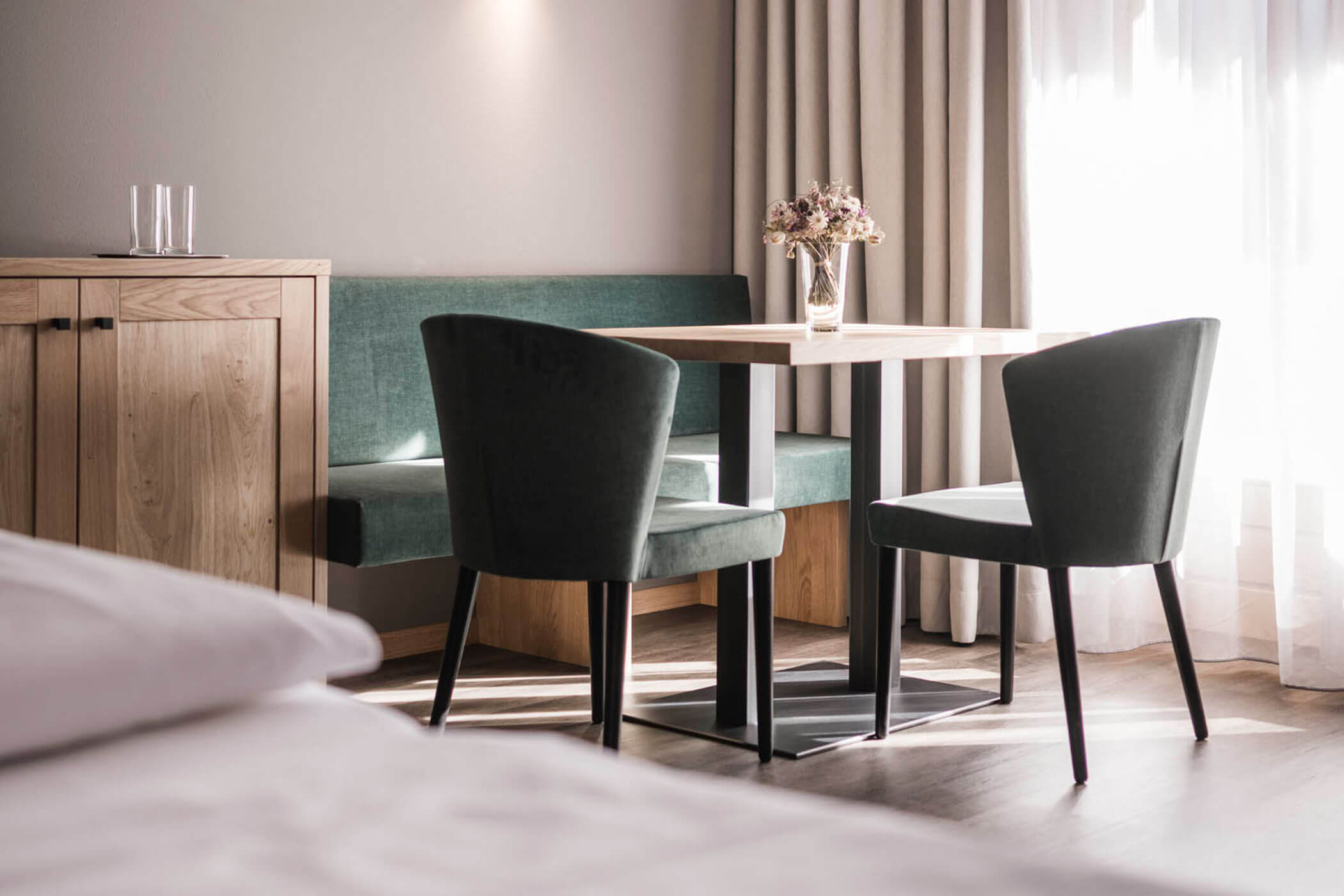 Sitzecke im Spitzen Zimmer mit grünen Stühlen, Bank und Holztisch, darauf ein kleiner Blumenstrauß - Hotel Alpenhof